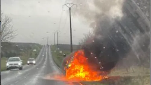 Une voiture en feu le long de la route